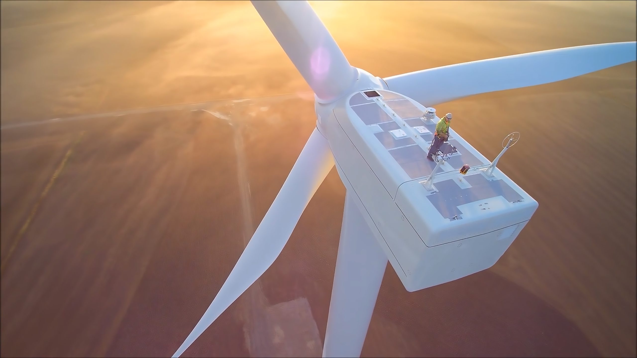 Un aerogenerador visto desde arriba al atardecer. Un trabajador está encima